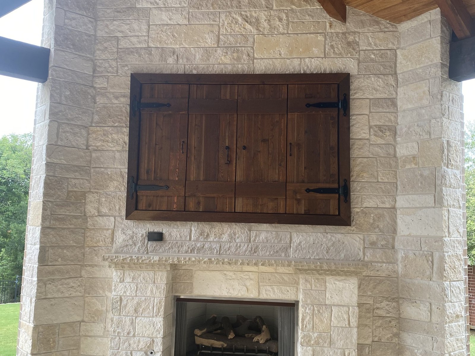 Covered outdoor living space with stone fireplace, built-in grill and flagstone patio at dusk